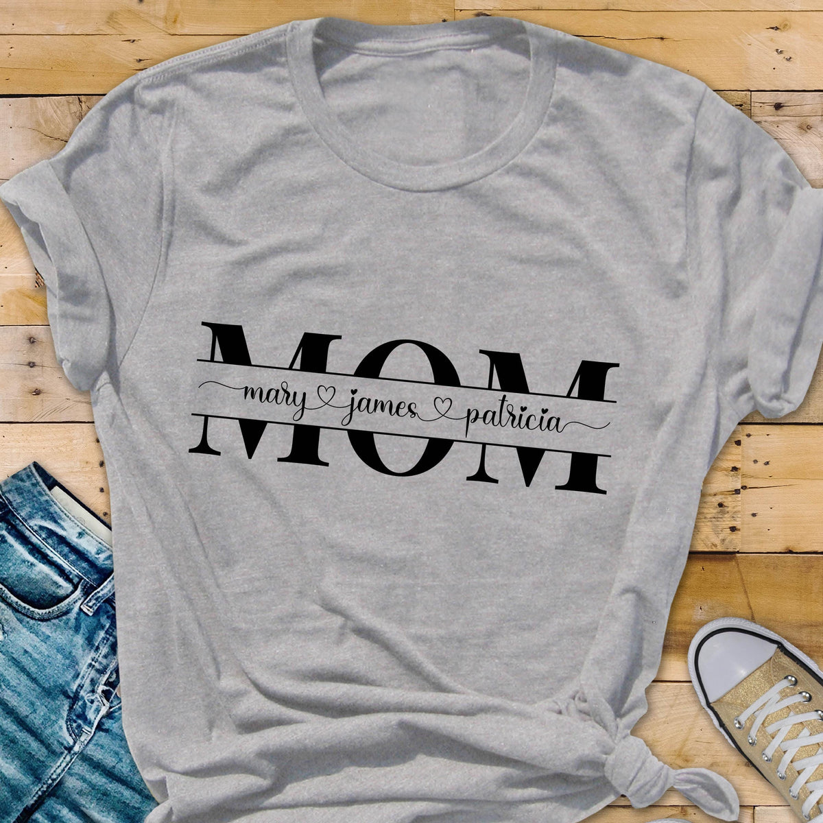 May include: Gray t-shirt with the word "MOM" in black letters. The word "MOM" is surrounded by a black line with the names "mary", "james", and "patricia" written in cursive with a heart symbol between each name.