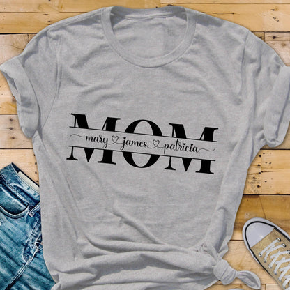 May include: Gray t-shirt with the word "MOM" in black letters. The word "MOM" is surrounded by a black line with the names "mary", "james", and "patricia" written in cursive with a heart symbol between each name.