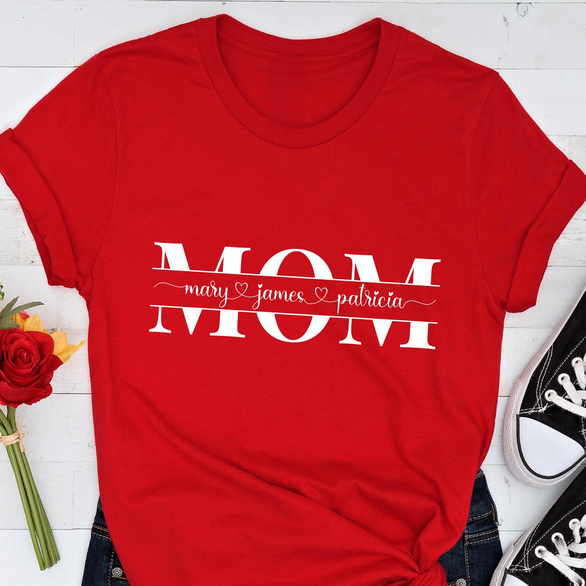 May include: Red t-shirt with the word "MOM" in white letters with a banner underneath that reads "mary ♥ james ♥ patricia".
