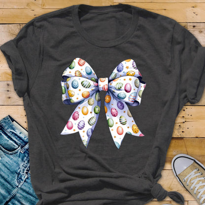 May include: A dark gray t-shirt with a white bow printed on the front. The bow is decorated with colorful Easter eggs.