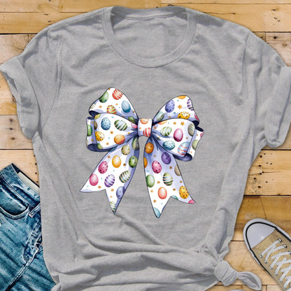 May include: A gray t-shirt with a white bow printed on the front. The bow is decorated with colorful Easter eggs.