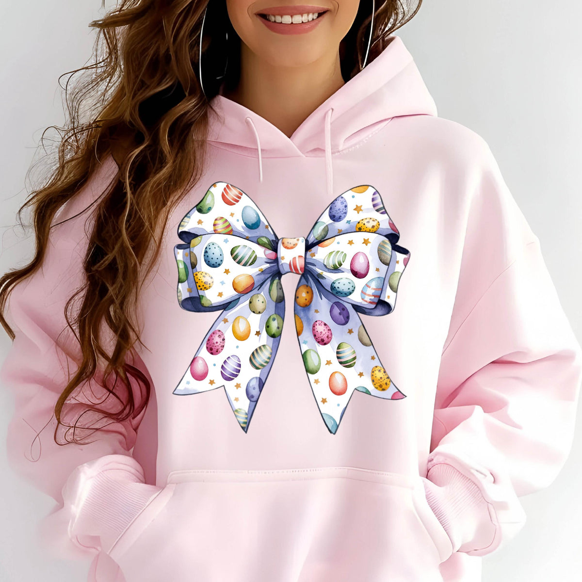 May include: Pink hoodie with a large white bow printed on the front. The bow is decorated with colorful Easter eggs.
