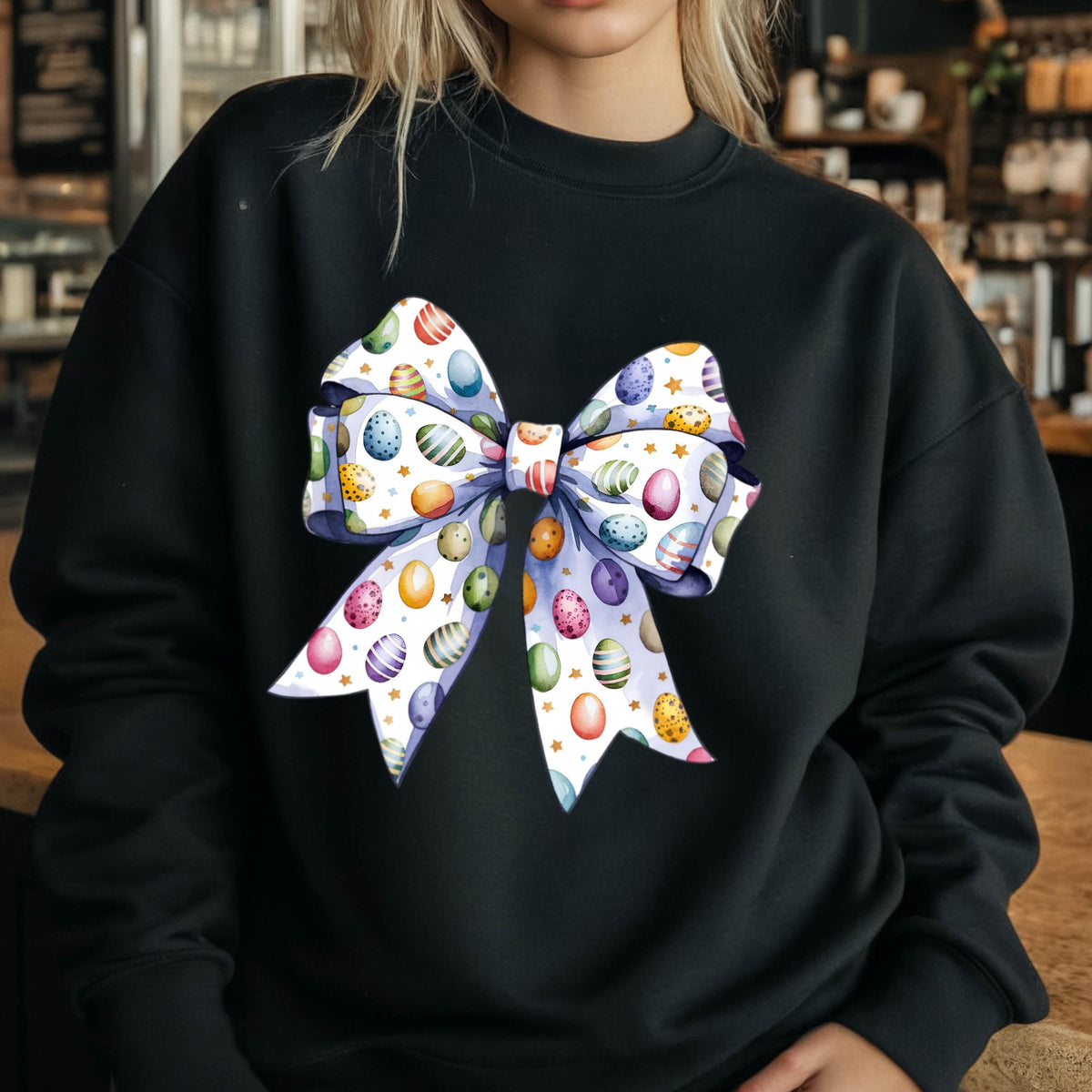 May include: Black sweatshirt with a white bow printed on the front. The bow is decorated with colorful Easter eggs.
