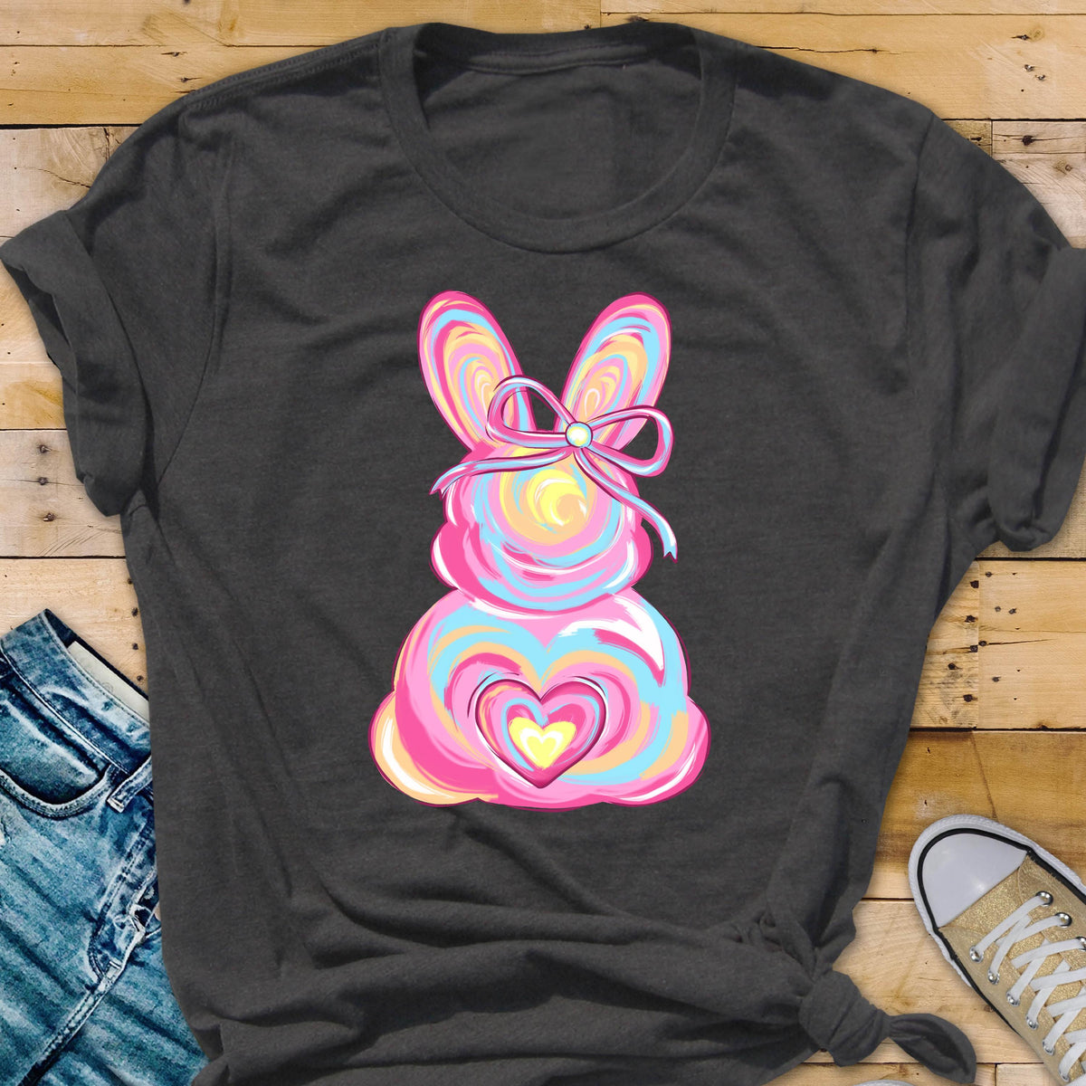 May include: A dark gray t-shirt with a pink and blue swirl design of an Easter bunny with a bow. The bunny has a yellow heart in the center of its chest.