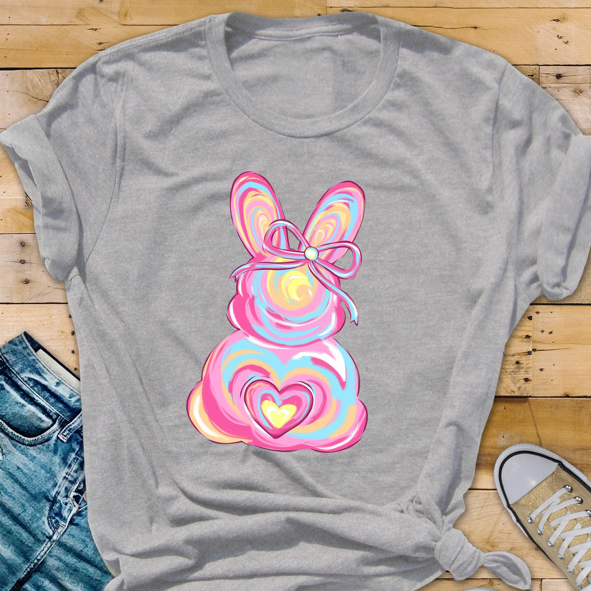 May include: A gray t-shirt with a pink, blue, and yellow Easter bunny design. The bunny has a bow and a heart on its chest.