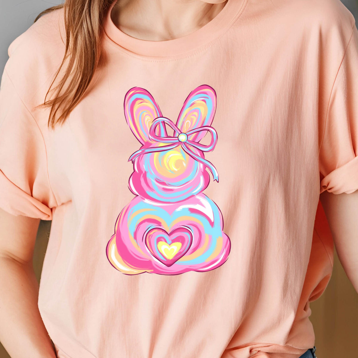 May include: A pink t-shirt with a colorful abstract bunny design. The bunny has a pink bow and a yellow heart in its center.