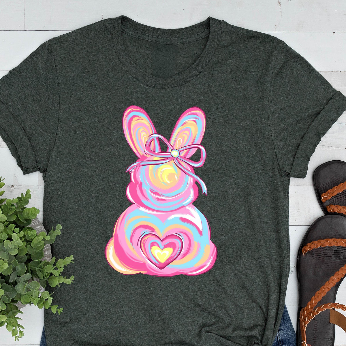 May include: A dark green t-shirt with a pink, blue, and yellow swirl design of an Easter bunny with a pink bow. The bunny has a pink heart with a yellow center.