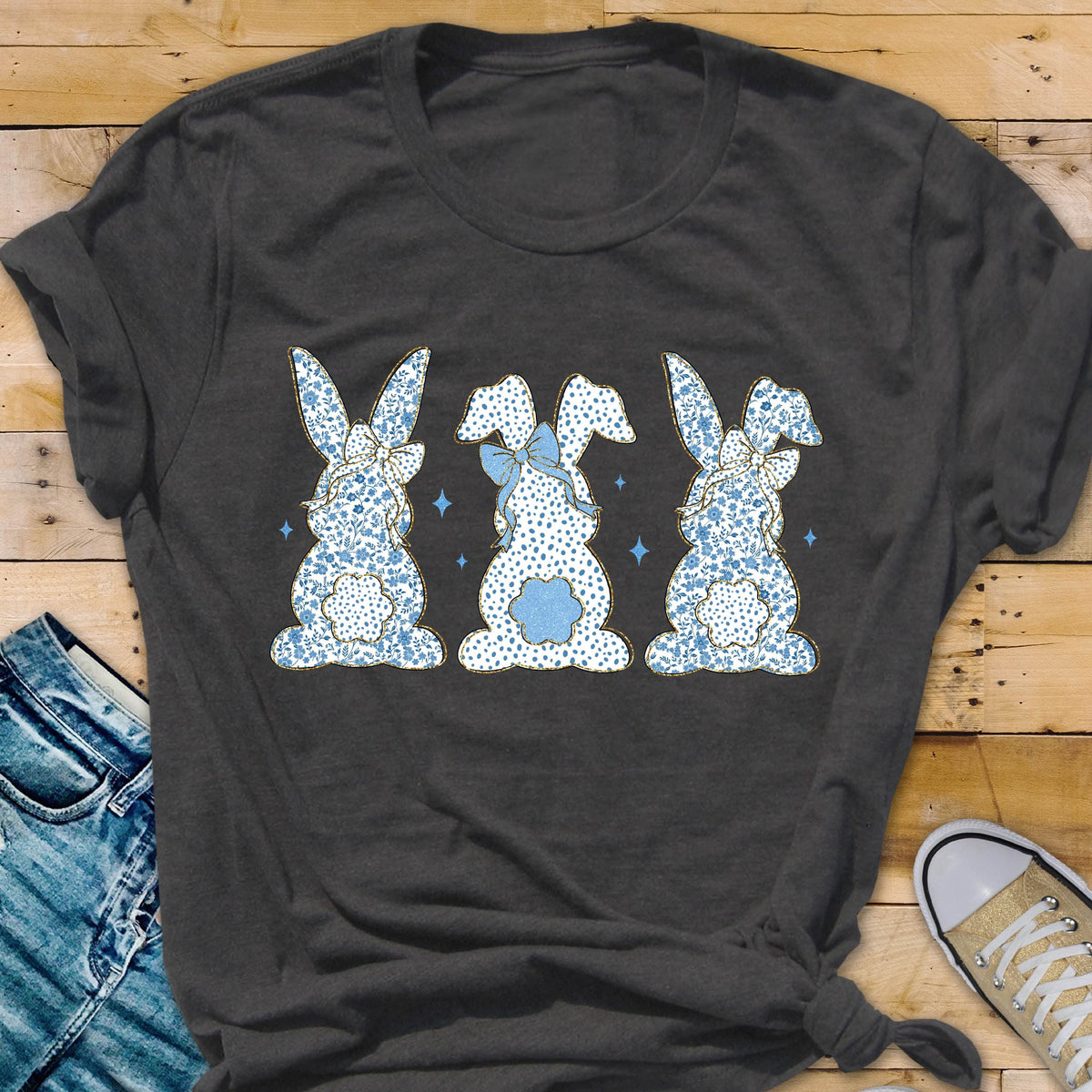 May include: A dark gray t-shirt with a graphic of three blue bunnies with blue bows and white polka dots. The bunnies are facing away from the viewer.