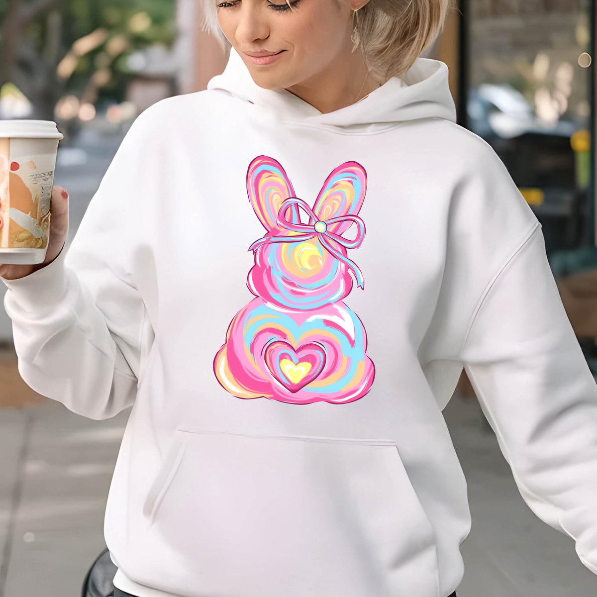 May include: White hoodie with a pink and blue abstract bunny design with a bow. The bunny has a heart in the center.