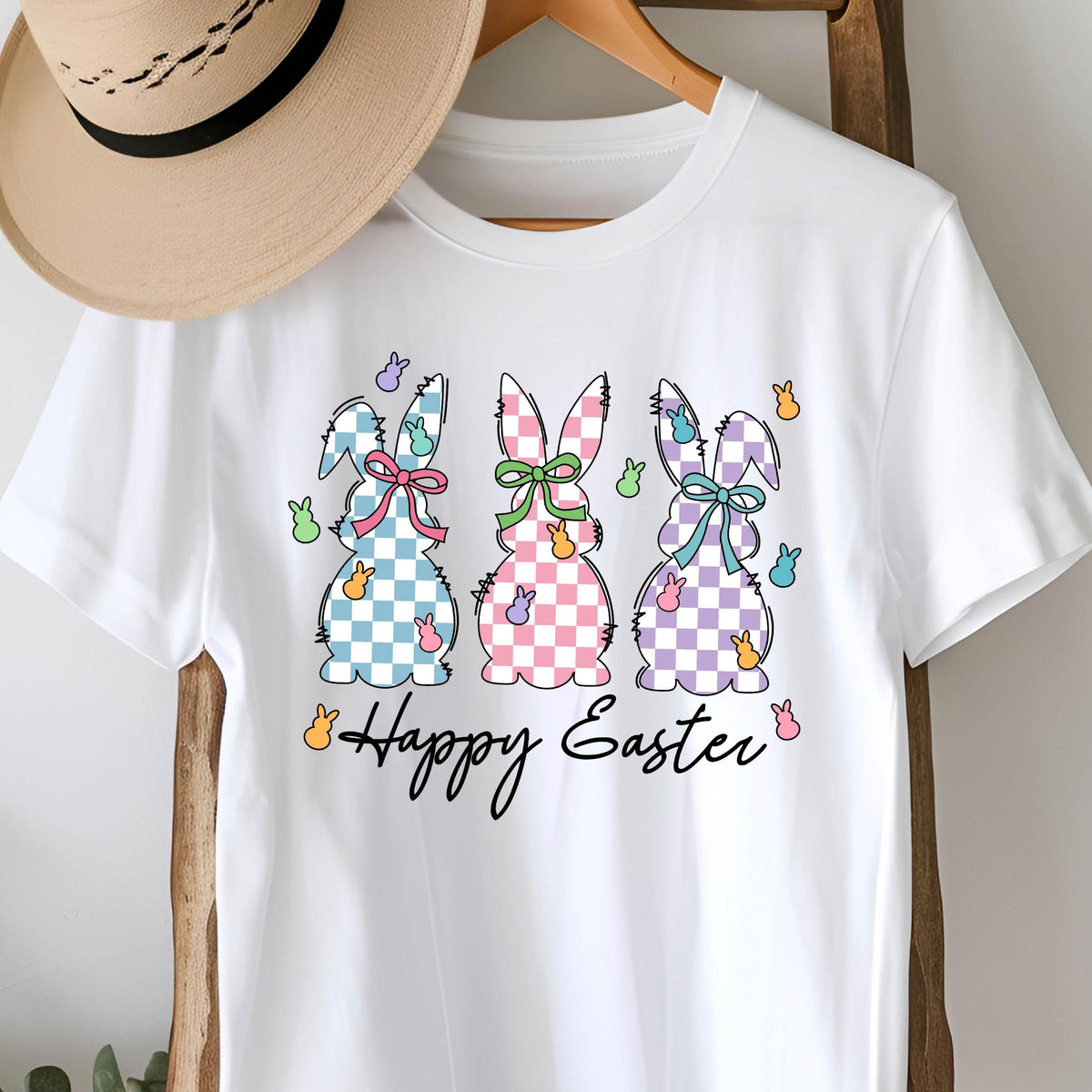 May include: White t-shirt with a graphic of three checkered Easter bunnies and the text "Happy Easter".