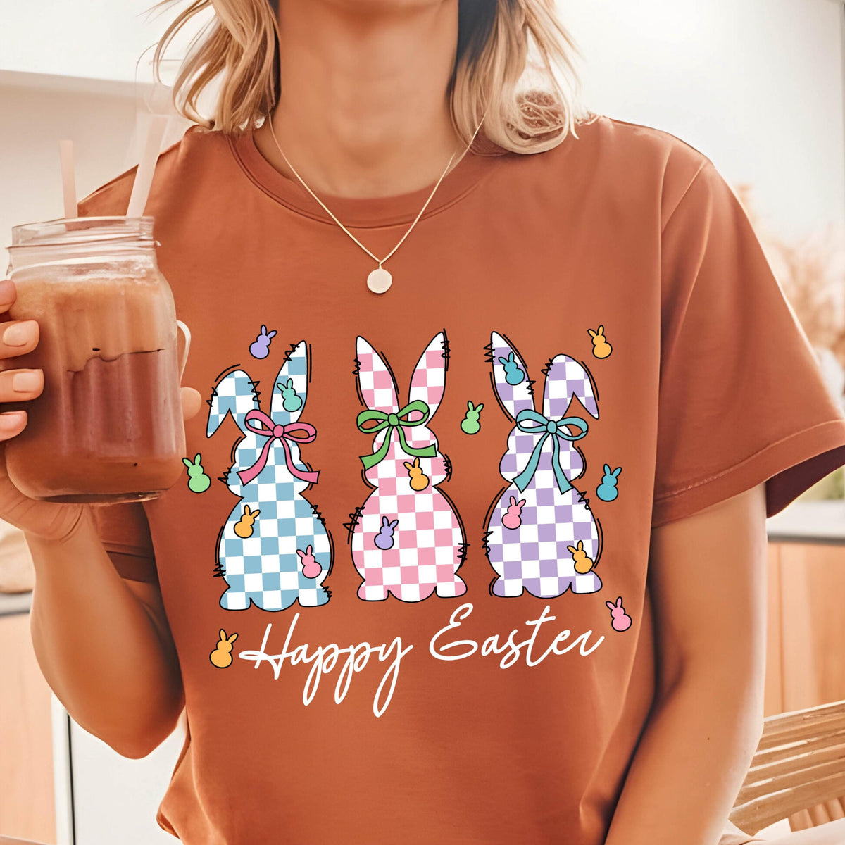 May include: A brown t-shirt with a graphic of three pastel checkered bunnies with bows and the text "Happy Easter".