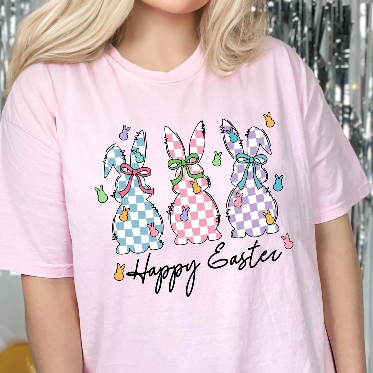 May include: Pink t-shirt with a graphic of three checkered Easter bunnies and the text "Happy Easter".