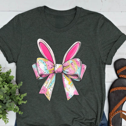 May include: A dark green t-shirt with a pink and white bow with bunny ears. The bow has a colorful abstract pattern.