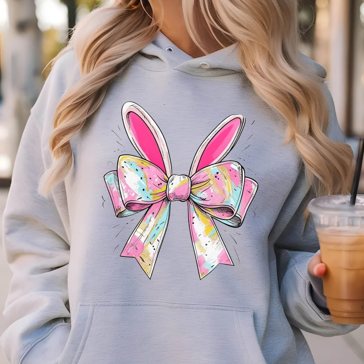 May include: A gray hoodie with a pink and white bow with bunny ears on the front. The bow has a colorful, watercolor-like design.
