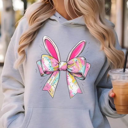 May include: A gray hoodie with a pink and white bow with bunny ears on the front. The bow has a colorful, watercolor-like design.