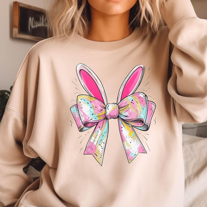 May include: A light brown sweatshirt with a colorful bow and bunny ears graphic print. The bow is pink, blue, yellow, and white with a swirl pattern. The bunny ears are pink.