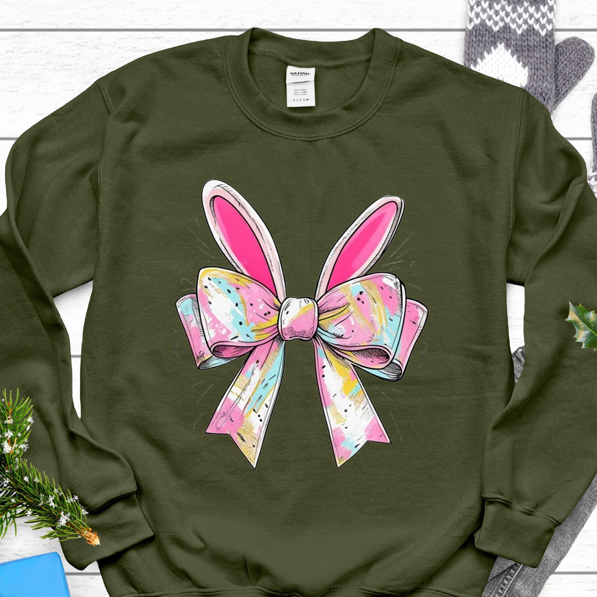 May include: A green sweatshirt with a pink and white bow with bunny ears. The bow has a colorful, abstract pattern.
