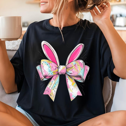 May include: Black t-shirt with a colorful bow and bunny ears design. The bow is pink, yellow, blue, and white. The bunny ears are pink.