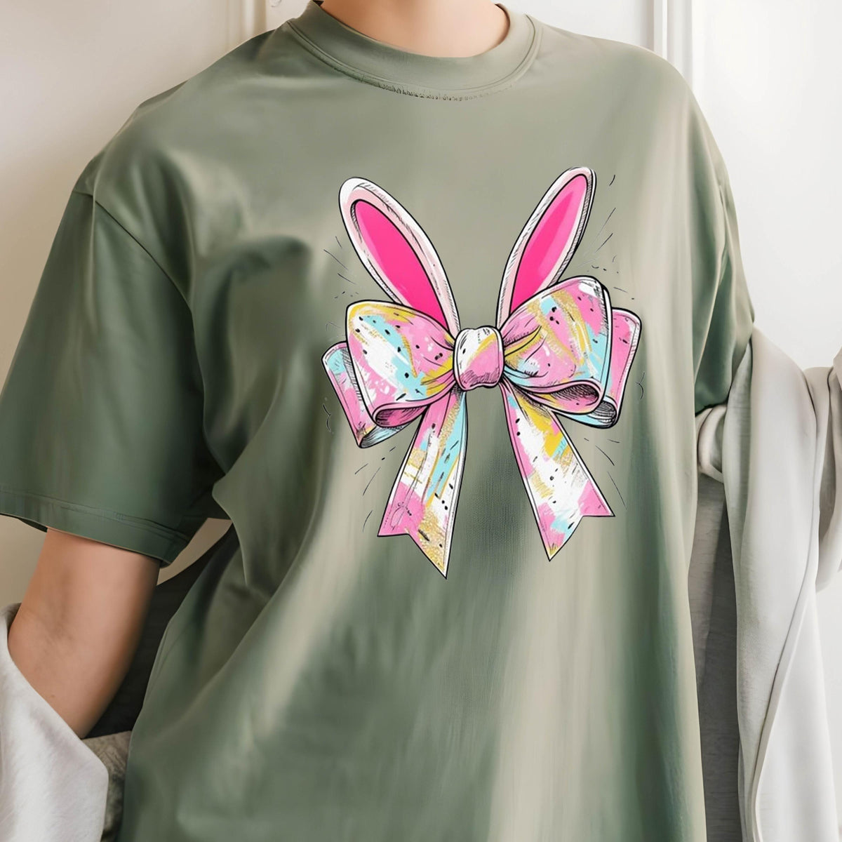 May include: A green t-shirt with a pink and white bow with bunny ears printed on the front.