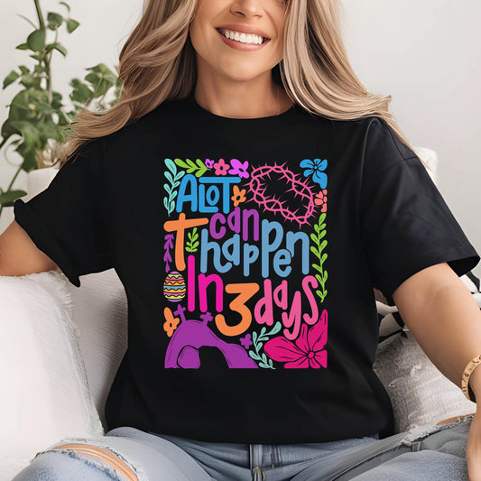 May include: A black t-shirt with a colorful graphic design that says "A lot can happen in 3 days". The graphic includes a cross, a crown of thorns, an Easter egg, and a tomb.