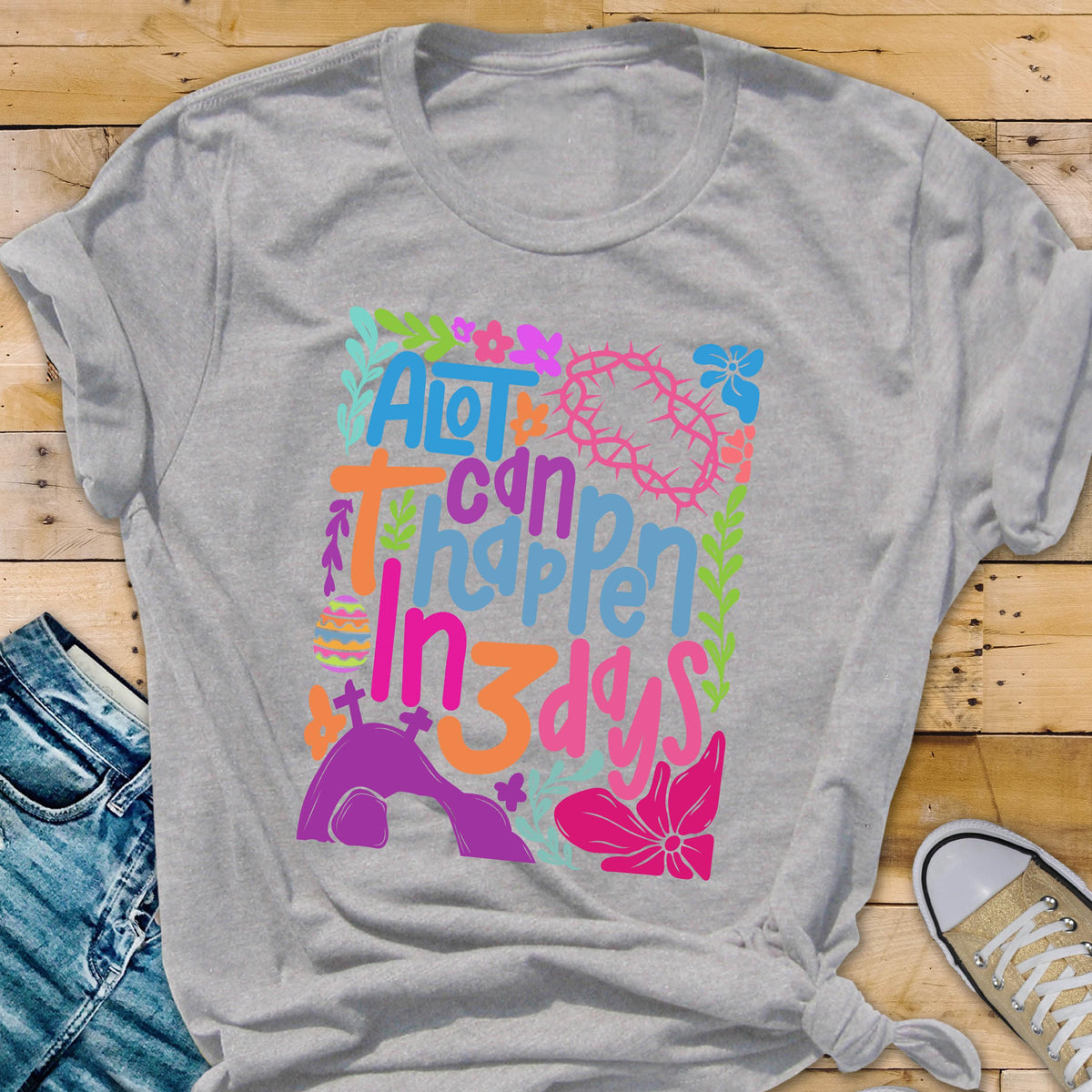 May include: A gray t-shirt with a colorful graphic design that says "A lot can happen in 3 days". The graphic includes flowers, a cross, a crown of thorns, and a tomb.