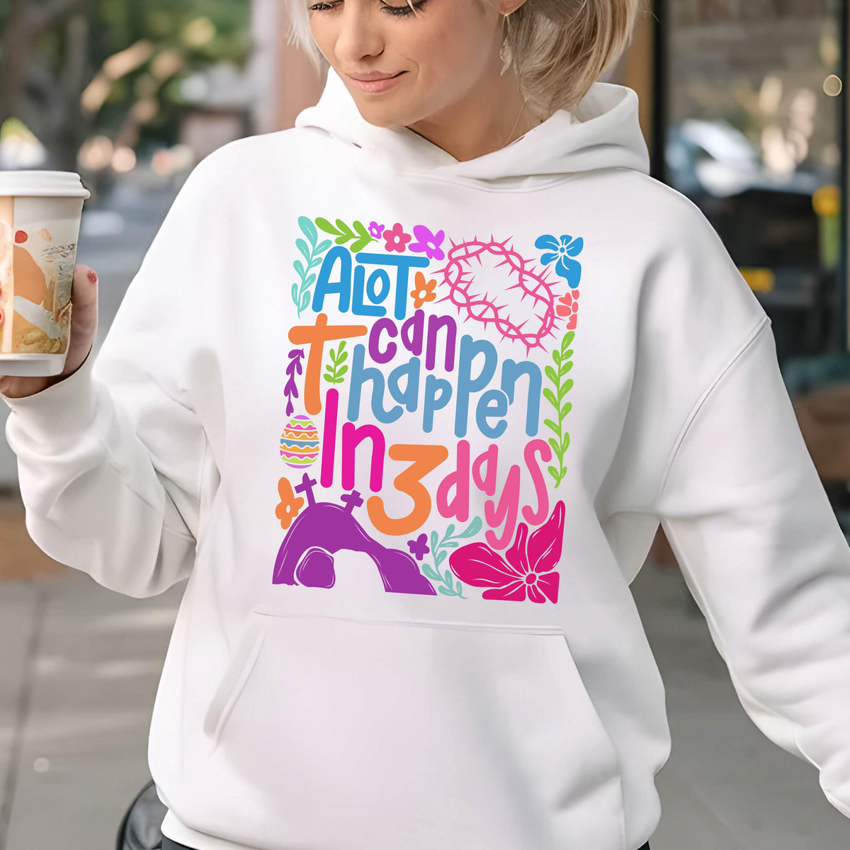 May include: White hoodie with a colorful graphic design that says "A lot can happen in 3 days". The graphic includes flowers, a cross, and an Easter egg.
