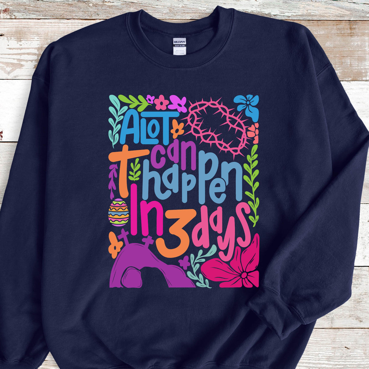 May include: A navy blue sweatshirt with a colorful graphic design that says "A lot can happen in 3 days". The graphic includes flowers, a crown of thorns, a cross, and an Easter egg.