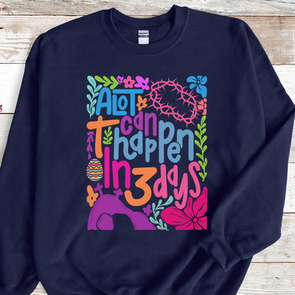 May include: A navy blue sweatshirt with a colorful graphic design that says "A lot can happen in 3 days". The graphic includes flowers, a crown of thorns, a cross, and an Easter egg.