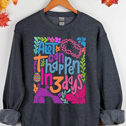 May include: A dark gray sweatshirt with a colorful graphic design that says "A lot can happen in 3 days". The graphic features flowers, leaves, and a crown of thorns.
