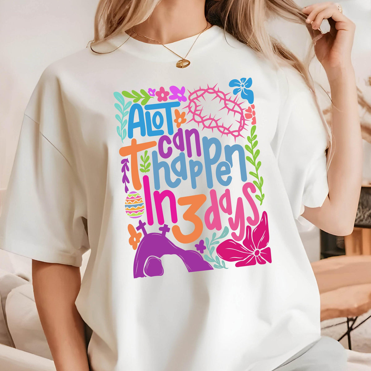 May include: White t-shirt with a colorful graphic design that says "A lot can happen in 3 days". The design includes flowers, a cross, a crown of thorns, and an Easter egg.