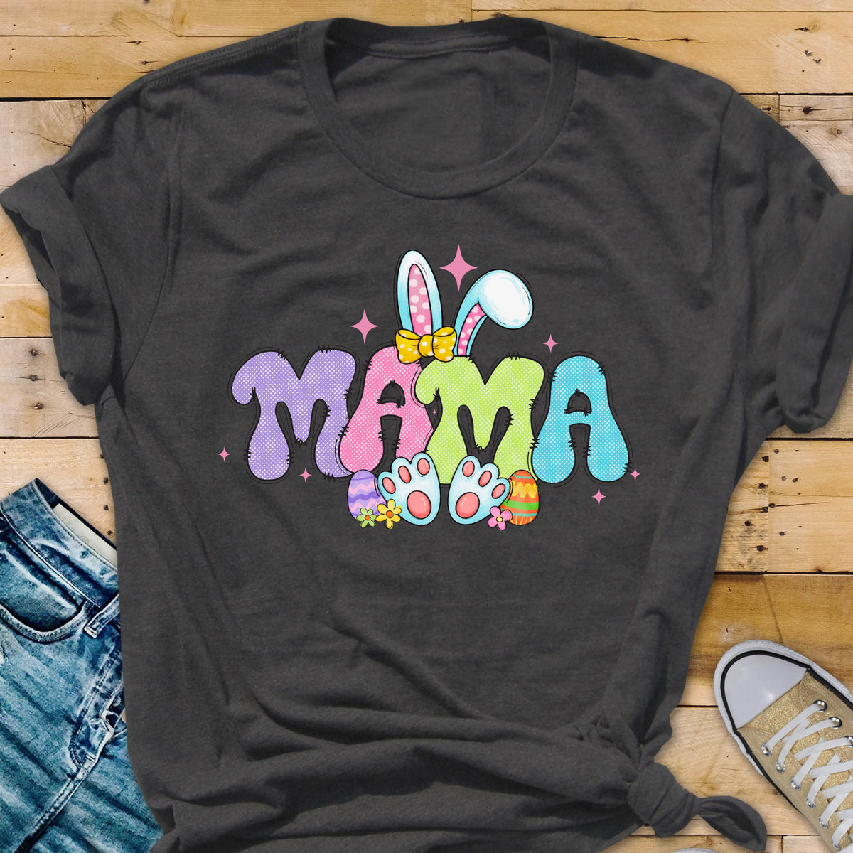 May include: A dark grey t-shirt with a colorful graphic of a bunny with the word "MAMA" in a playful font. The bunny is wearing a pink bow and holding Easter eggs.