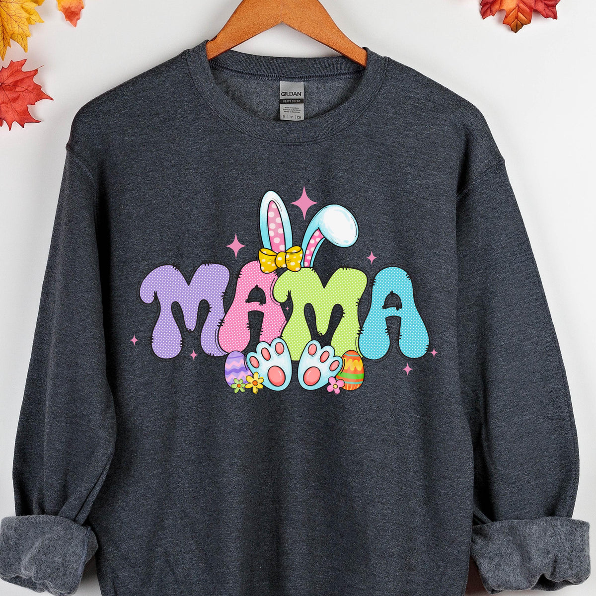 May include: A dark gray sweatshirt with a colorful Easter bunny graphic and the word "MAMA" in a playful font. The bunny is wearing a pink bow and holding Easter eggs.