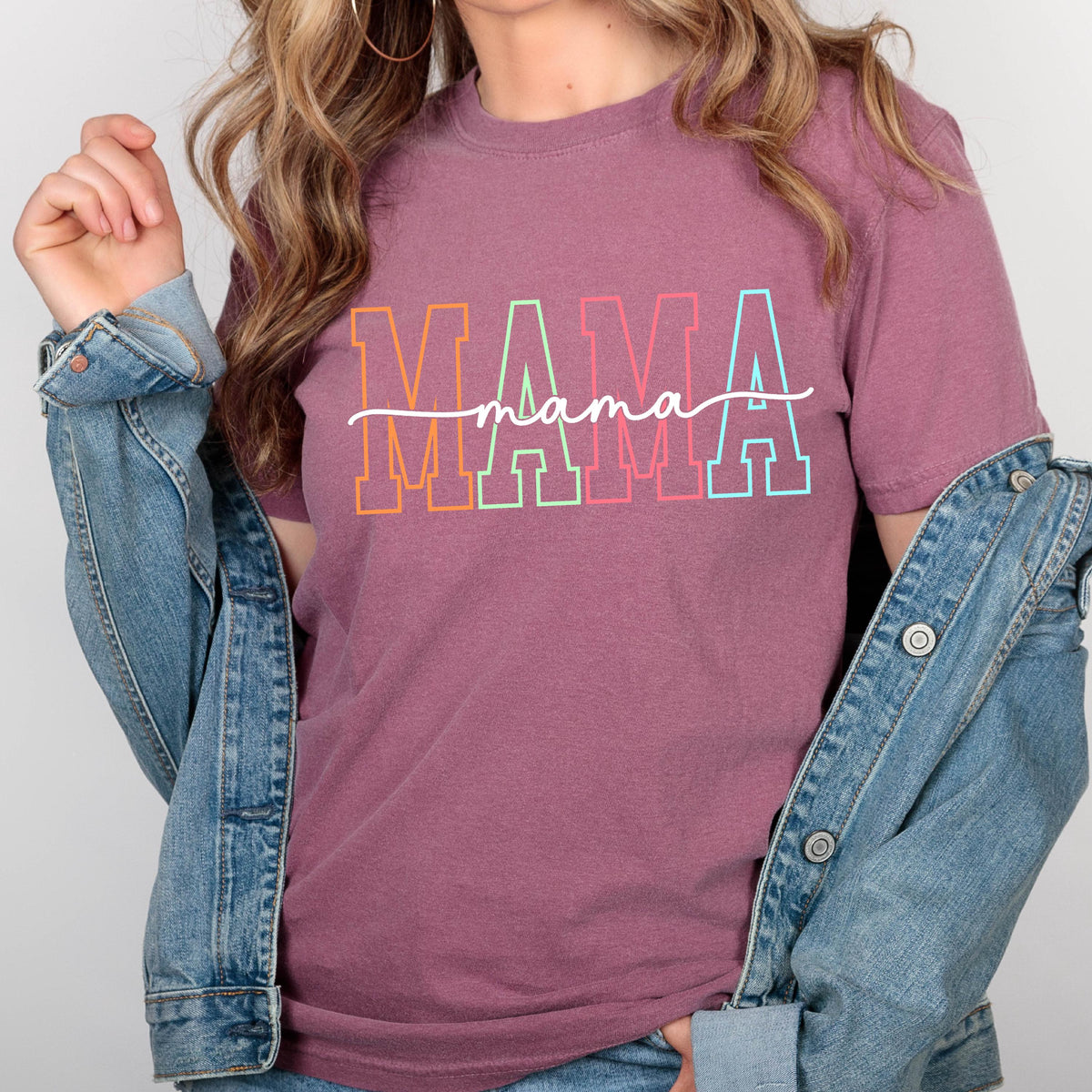 May include: A mauve colored t-shirt with the word "MAMA" in rainbow colored letters with a script font "mama" underneath.