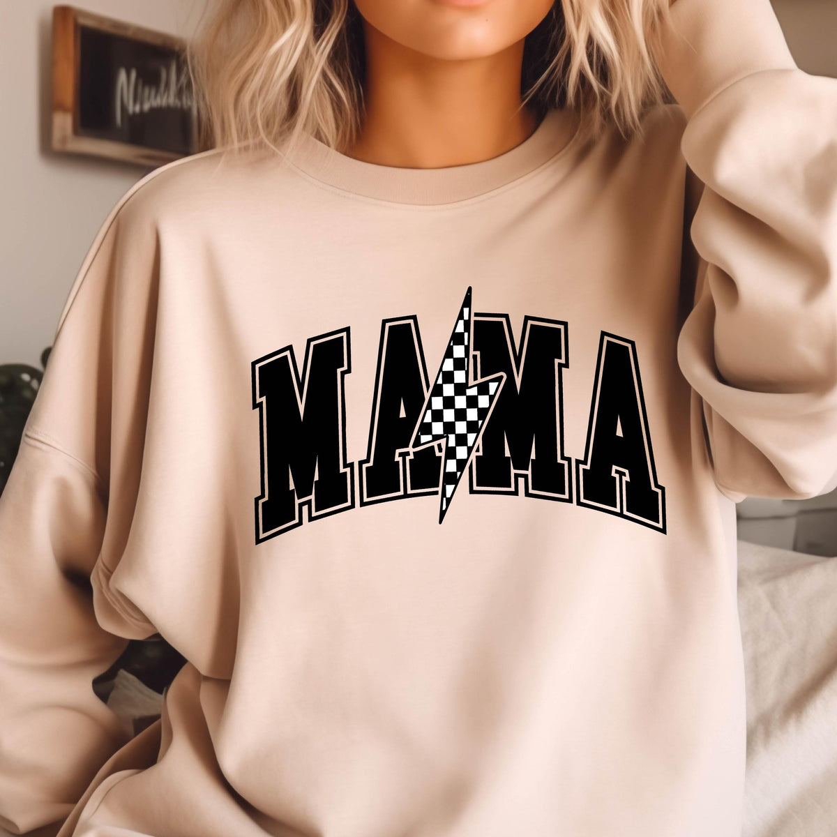 May include: A light beige sweatshirt with a black graphic print of the word "MAMA" with a checkered lightning bolt in the center.