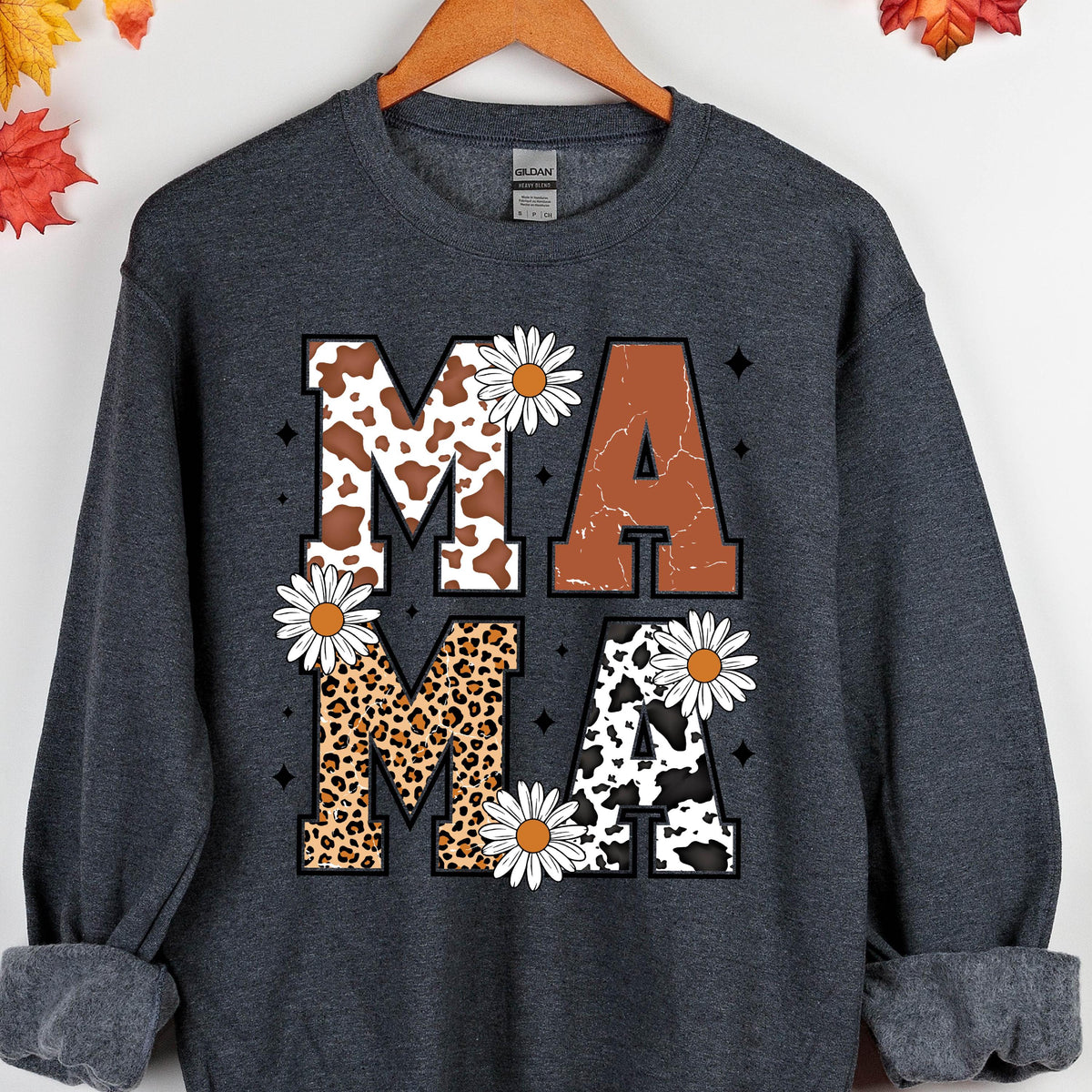 May include: A dark gray sweatshirt with the word "MAMA" printed on the front. The letters are made up of different animal prints, including cow, leopard, and cheetah. There are white daisies around the letters.
