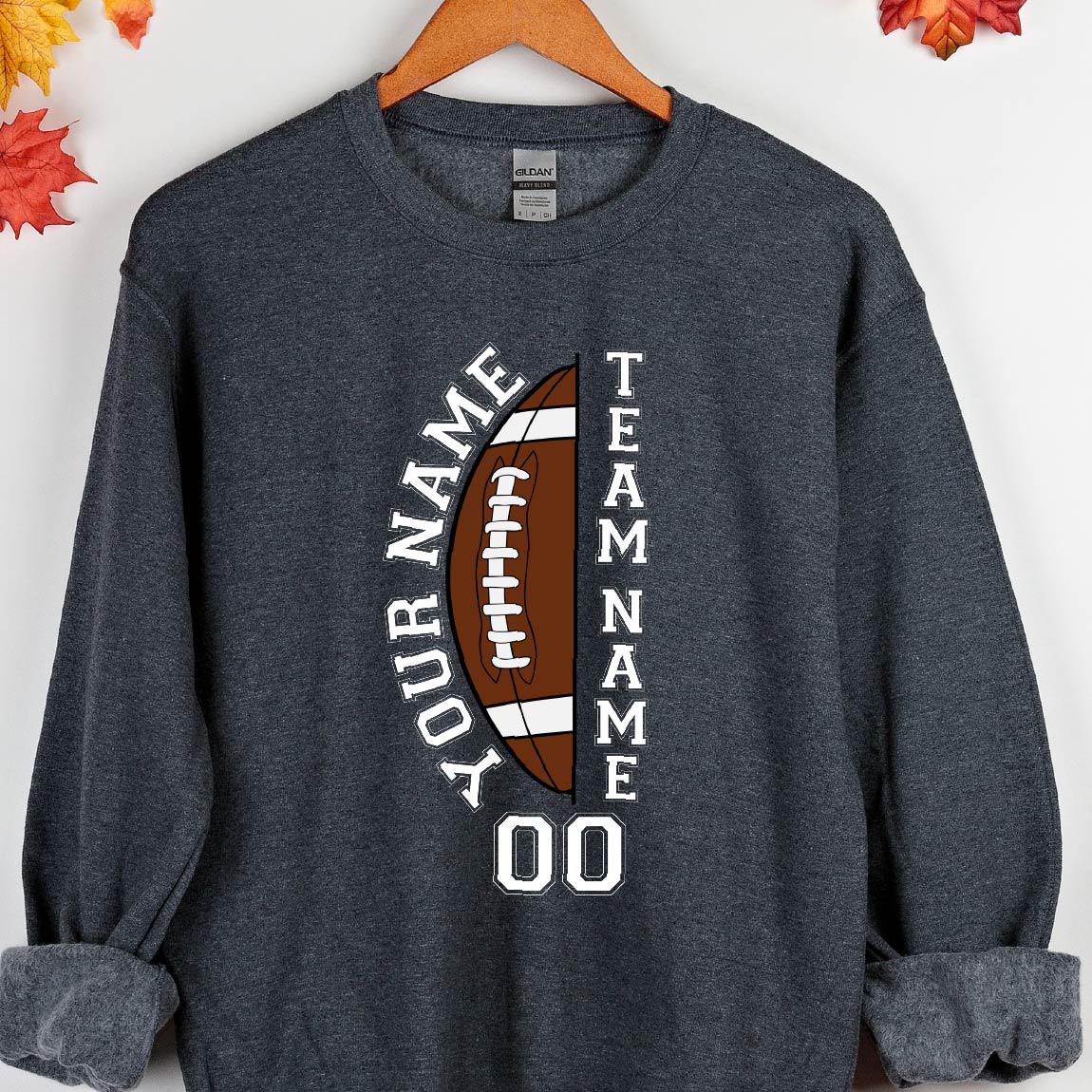 May include: Dark gray sweatshirt with a football design. The design includes a brown football with white details, the words "YOUR NAME" and "TEAM NAME" in white, and the number "00". The sweatshirt is hanging on a wooden hanger.