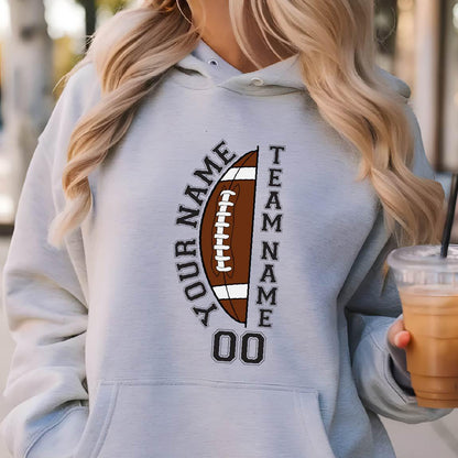 May include: Light gray hoodie with a football graphic. The design includes a brown football with white laces, the words "YOUR NAME" and "TEAM NAME" in black, and the number "00". The hoodie has a drawstring hood.