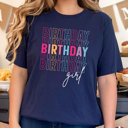 May include: Navy blue t-shirt with the word "BIRTHDAY" stacked in a colorful, retro font. The word "girl" is written in a cursive font below the stacked text. The shirt is a comfortable, casual style.