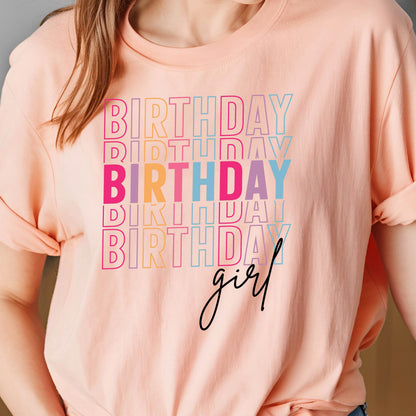May include: A peach-colored t-shirt with the word "BIRTHDAY" repeated in a stacked design. The word "BIRTHDAY" is in various colors, including pink, orange, blue, and purple. The word "girl" is written in a cursive font.