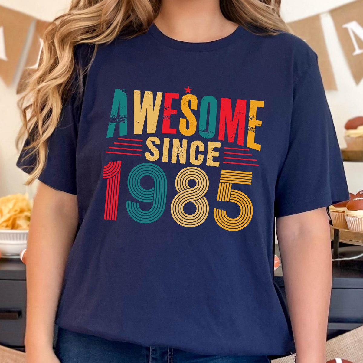 May include: A navy blue t-shirt with the text "Awesome Since 1985" in a retro style font with colorful stripes. 