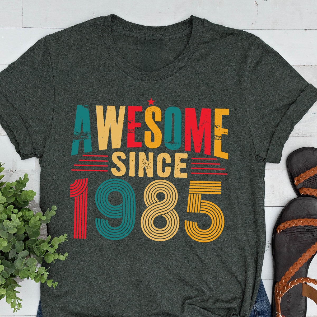 May include: A dark green t-shirt with the text "Awesome Since 1985" in colorful retro-style lettering.