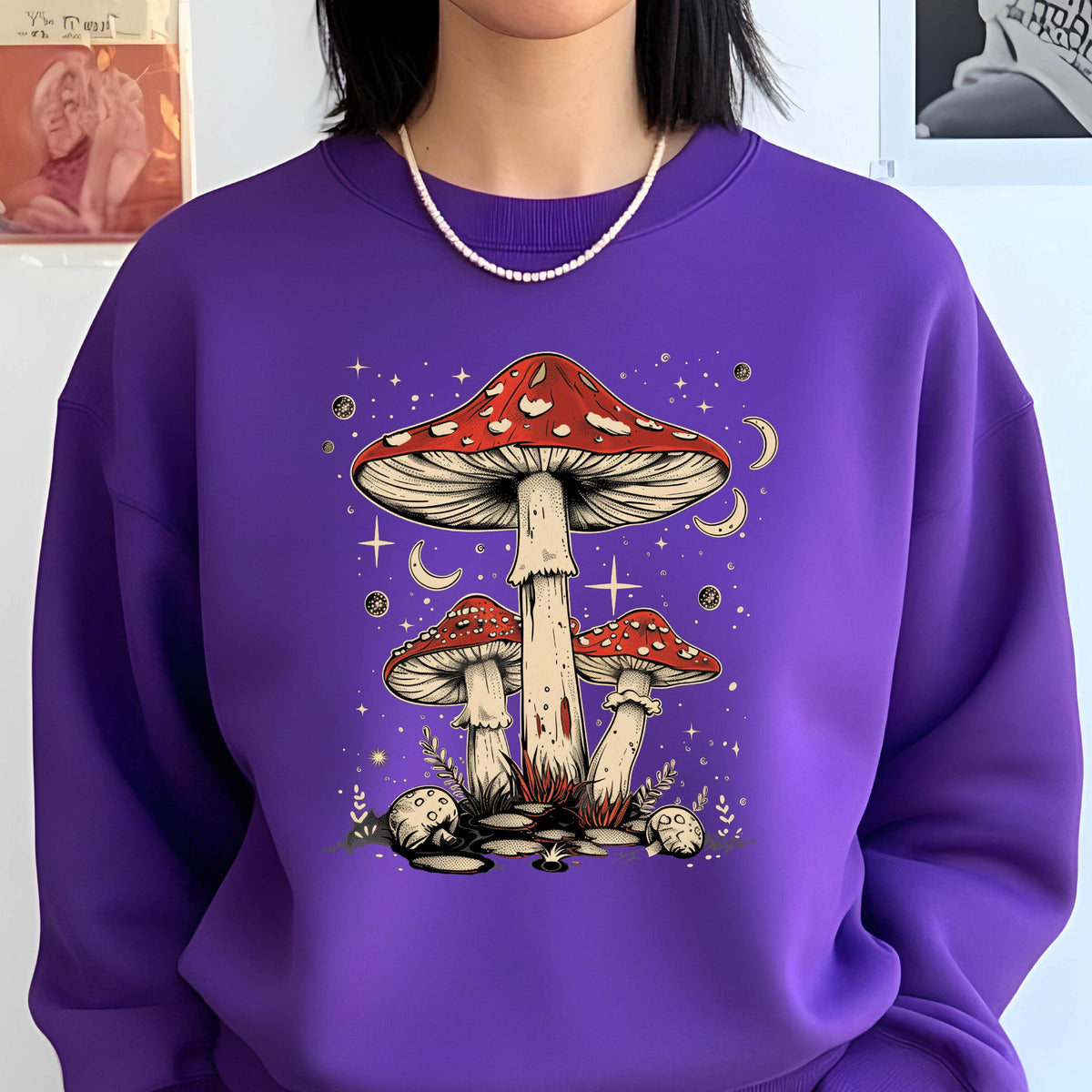 May include: Purple sweatshirt with a graphic of three red and white mushrooms with white stems against a dark purple background with white stars and crescent moons.
