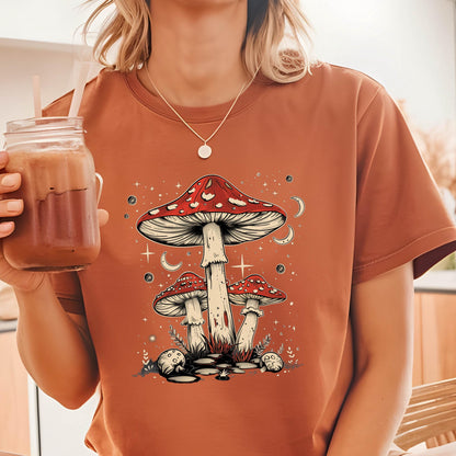 May include: A rust-colored t-shirt with a graphic of three red and white mushrooms with white stems against a dark blue background with white stars and crescent moons.