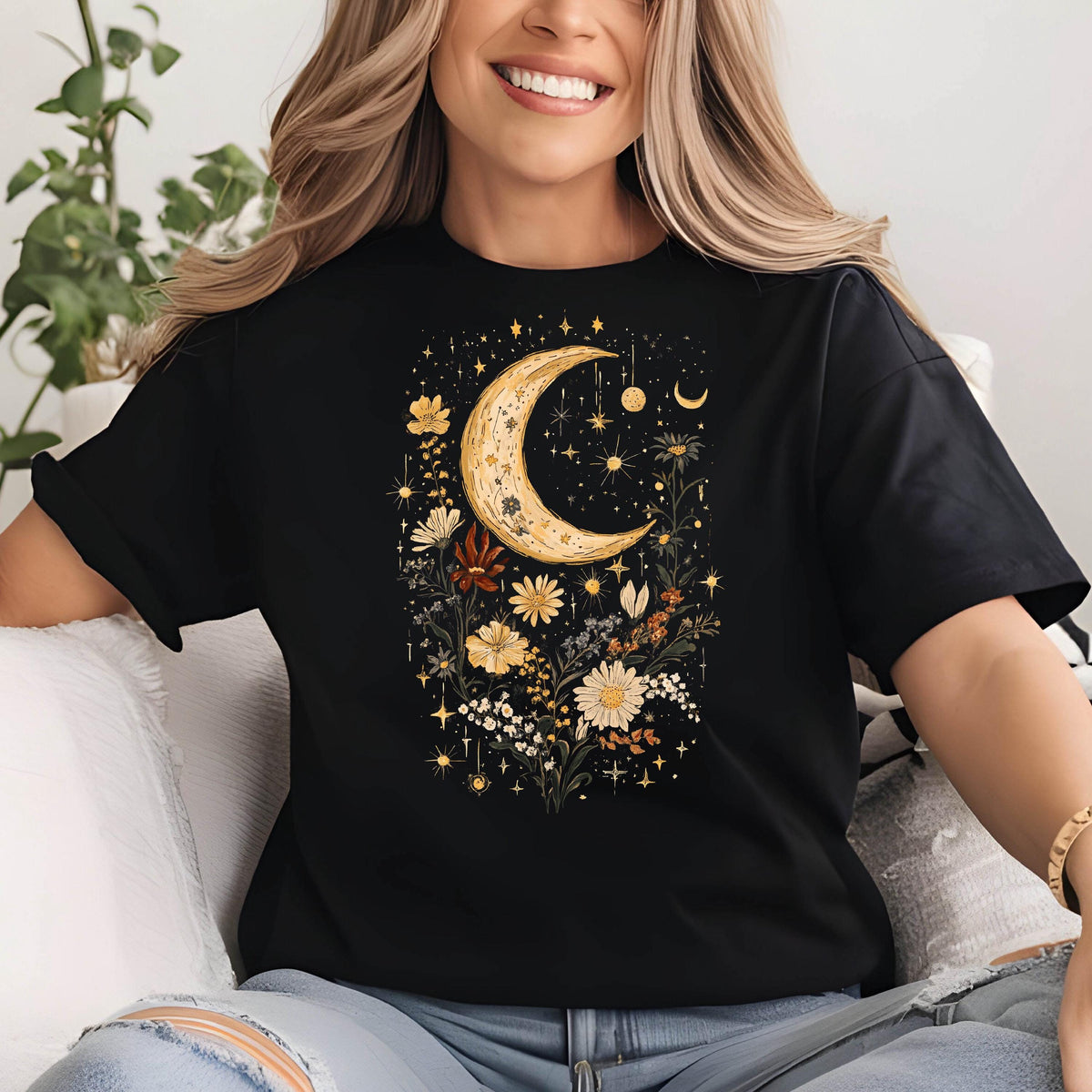 May include: Black t-shirt featuring a celestial design. The graphic includes a crescent moon, stars, and various flowers in shades of yellow, white, and brown. The design is centered on the front of the shirt.