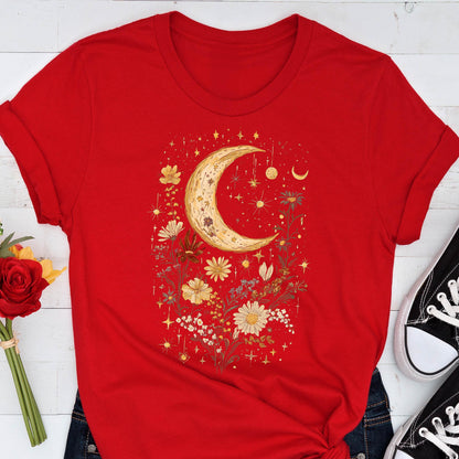 May include: A red t-shirt featuring a celestial design. The graphic includes a golden crescent moon, stars, and various flowers. The shirt is paired with blue jeans and black sneakers.