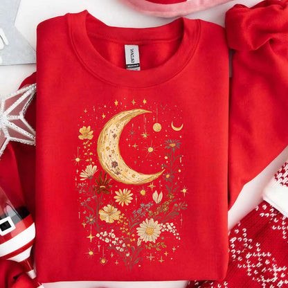 May include: A bright red crewneck sweatshirt featuring a central graphic of a large, textured crescent moon surrounded by various wildflowers and small, sparkling stars. The design is rendered in shades of yellow, gold, and white.