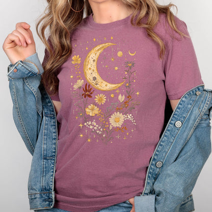 May include: A mauve t-shirt with a crescent moon and floral design in gold and yellow. The design features a crescent moon surrounded by flowers and stars.