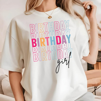 May include: White t-shirt with the text "Birthday" repeated in rainbow colors and the text "girl" in black script.