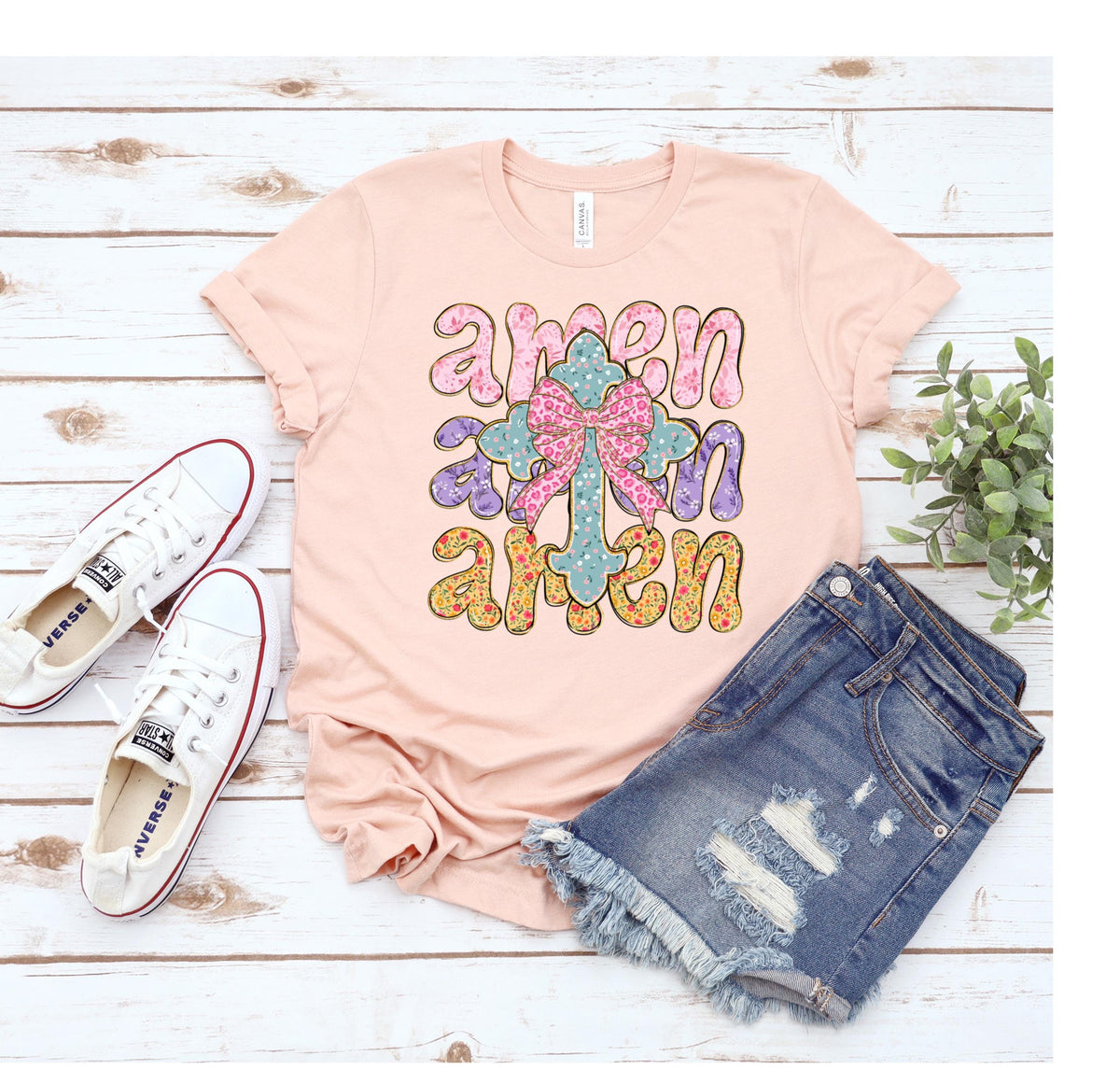 May include: A pink t-shirt with the word "amen" written three times in a colorful, stylized font. A floral cross with a pink bow is in the center of the design.