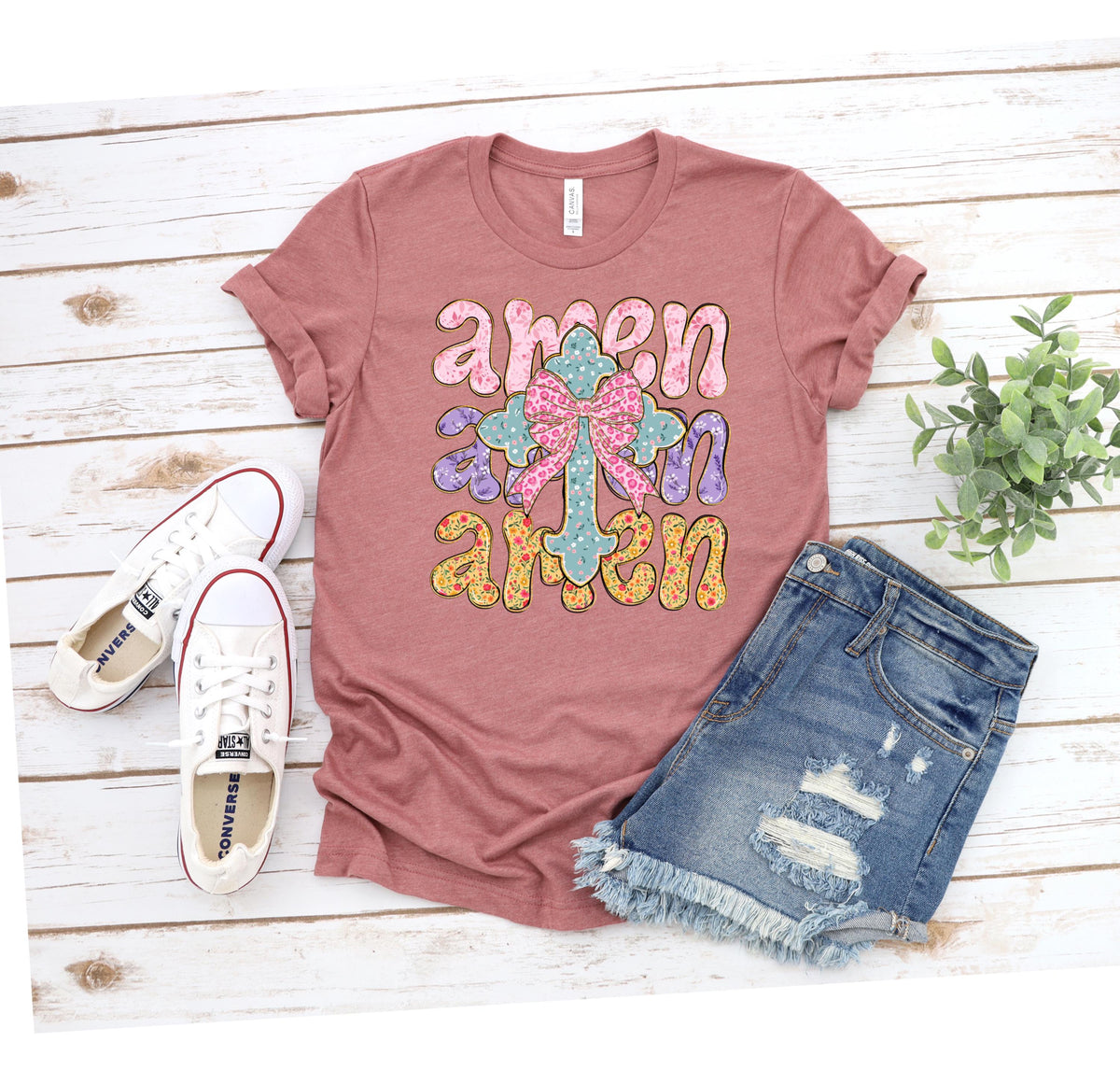 May include: A mauve t-shirt with a floral cross and the word "amen" repeated three times in a colorful, stylized font.